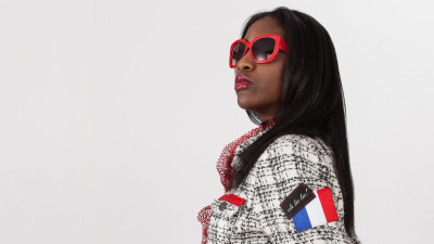 Black female model wearing a non military style peace jacket while posing on a white background.